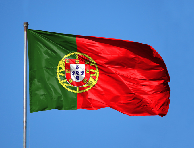 National flag of Portugal on a flagpole in front of blue sky.